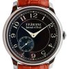 Close-up of a luxury wristwatch with a black dial, white numerals, and a brown leather strap.