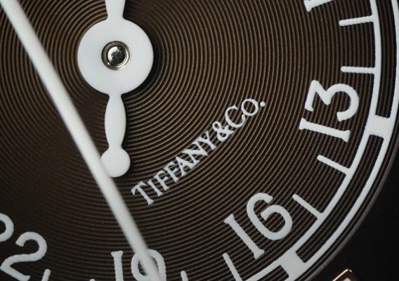 Close-up of a brown watch dial with white numerals and hands, featuring the Tiffany & Co branding visible on the face.