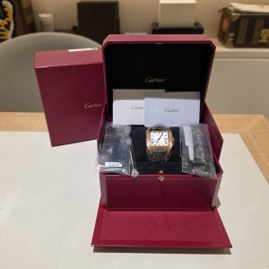 Cartier wristwatch in an open red Cartier presentation box with cards and accessories inside on a table.
