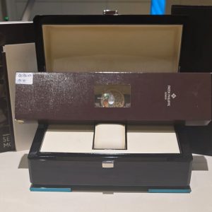 Patek Philippe watch in a burgundy display box with a small window, sitting on a black display case.