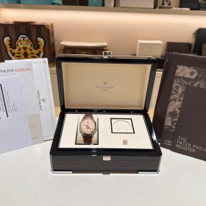 Open Patek Philippe presentation box with a rose‑dial watch and leather strap, surrounded by certificates and manuals on a showroom counter