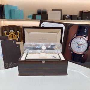 Patek Philippe wristwatch in an open wooden presentation box with papers on the left and a large watch poster on the right in a display setting.