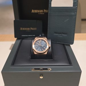 Audemars Piguet watch with a rose-gold case and blue dial in a green presentation box, with warranty card nearby.