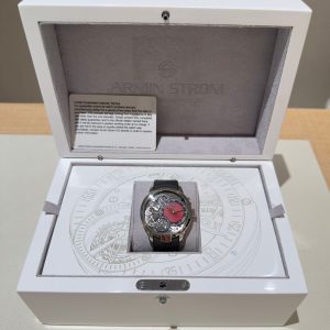 Armin Strom watch in a white display box with gray velvet interior and visible warranty card inside the lid edge.