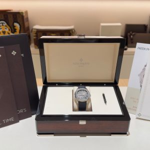 Patek Philippe watch in an open presentation box with accompanying brochures and booklets displayed around it on a white surface.
