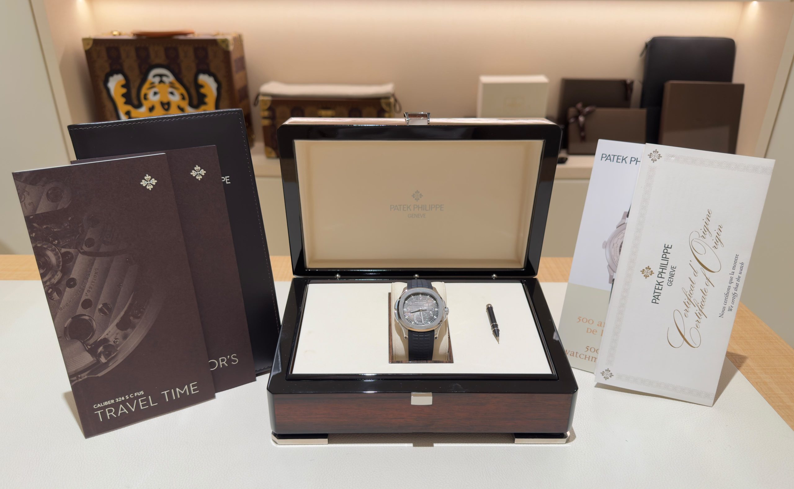 Patek Philippe watch in an open presentation box with accompanying brochures and booklets displayed around it on a white surface.