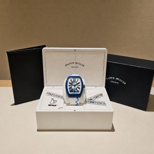 Franck Muller wristwatch in an open white presentation box with black outer boxes, on a beige surface.