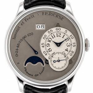 Close-up of a metallic wristwatch showing hours and minutes on a small dial, a date window reading 08, and a moon phase indicator.