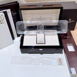 Patek Philippe watch in opened display box with clear plastic case and accompanying burgundy packaging boxes.